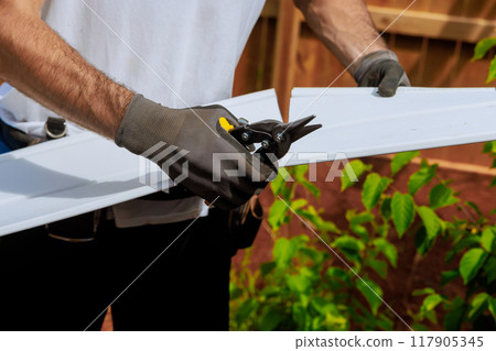 Craftsman cuts vinyl siding panel to desired size before installing it on facade of building Craftsman cuts vinyl siding panel to desired size before installing it on facade of building 117905345