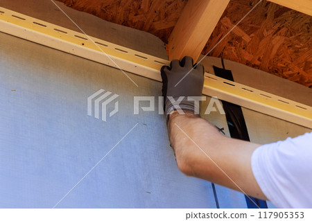 Craftsman nails J-channel vinyl trim before installing for siding in during construction house Craftsman nails J-channel vinyl trim before installing for siding in during construction house 117905353