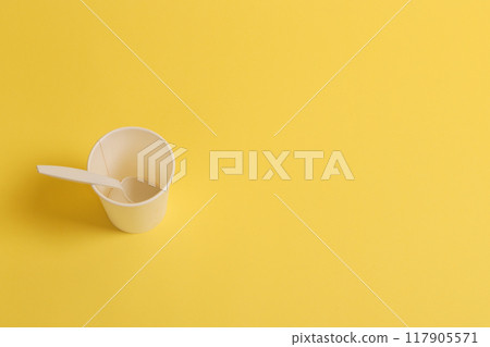 Disposable paper cup with a teaspoon on a yellow background. Disposable paper cup with a teaspoon on a yellow background. 117905571