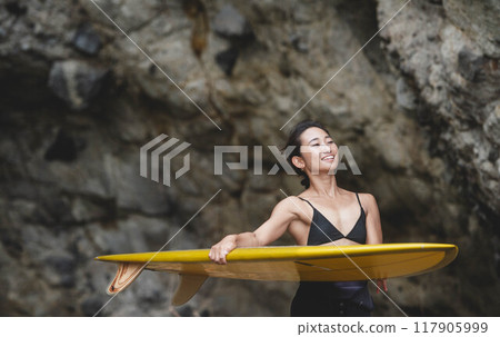在岩石地區拿著衝浪板的年輕女子 117905999