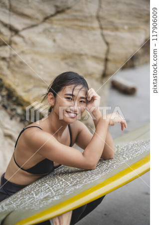 在岩石地區拿著衝浪板的年輕女子 117906009