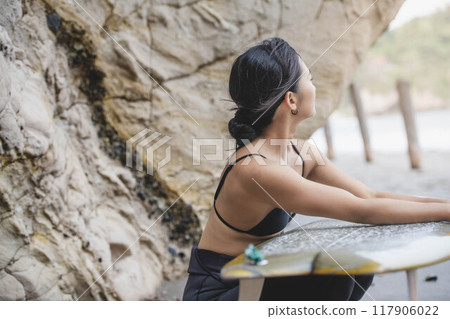 Young woman holding a surfboard on the rocks Young woman holding a surfboard on the rocks 117906022
