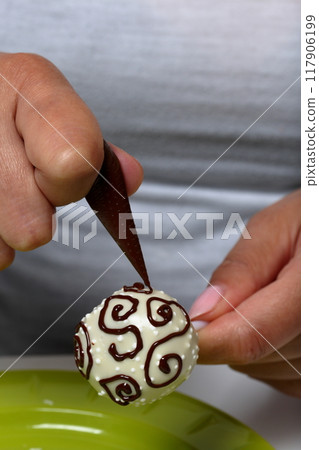 A woman decorates with the help of dark chocolate popcake glazed with white chocolate. A woman decorates with the help of dark chocolate popcake glazed with white chocolate. 117906199