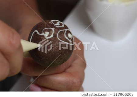 A woman decorates with the help of white chocolate popcake glazed with dark chocolate. A woman decorates with the help of white chocolate popcake glazed with dark chocolate. 117906202