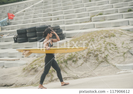 Young woman walking along the beach with a surfboard Young woman walking along the beach with a surfboard 117906612