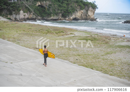 拿著衝浪板沿著海灘散步的年輕女子 117906616