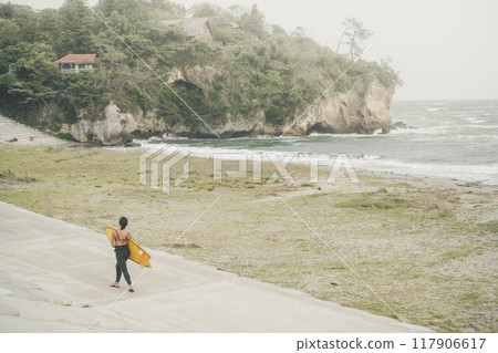 拿著衝浪板沿著海灘散步的年輕女子 117906617