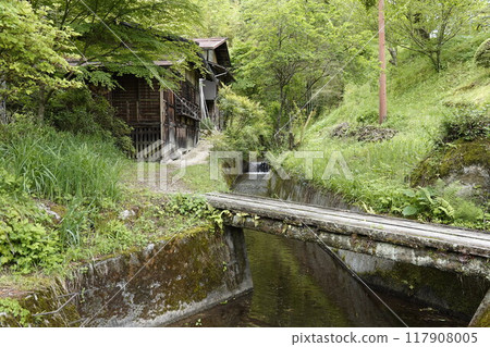 An old house in the mountains surrounded by beautiful fresh greenery and a spring waterway running alongside it 117908005