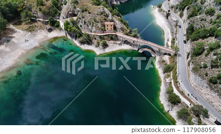 A serene aerial view of a picturesque bridge over turquoise waters near a charming abandoned building surrounded by rocky landscape A serene aerial view of a picturesque bridge over turquoise waters near a charming abandoned building surrounded by rocky landscape 117908056