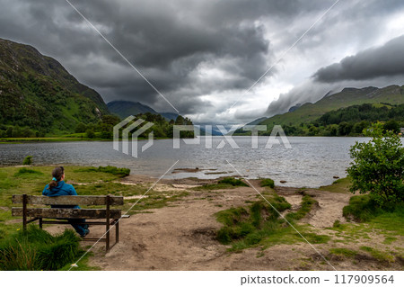 Woman On Bench Looking Over Lake Loch Shiel At Glenfinnan Monument On The Road To The Isles In Lochaber In Scotland, UK 117909564