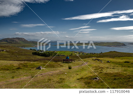 Single Woman On Bench Looks Over Atlantic Coast With Summer Isles, Isle Ristol And Eilean Mullagrach Near Village Altandhu In The Highlands Of Scotland, UK 117910046