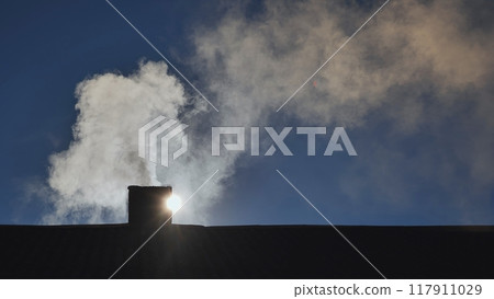 Silhouette of smoke against blue sky from the chimney of a village house. 117911029