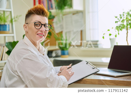 Portrait of smiling middle aged female mental therapist with clipboard in office Portrait of smiling middle aged female mental therapist with clipboard in office 117911142