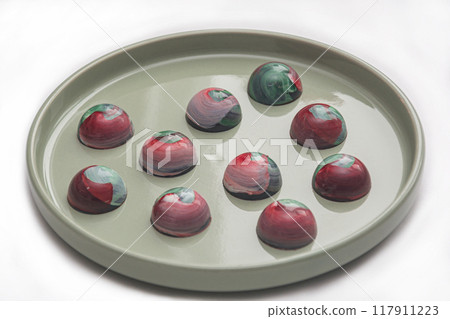 Collectible handmade tempered chocolate sweets with a glossy painted body on a round plate with blur elements 117911223
