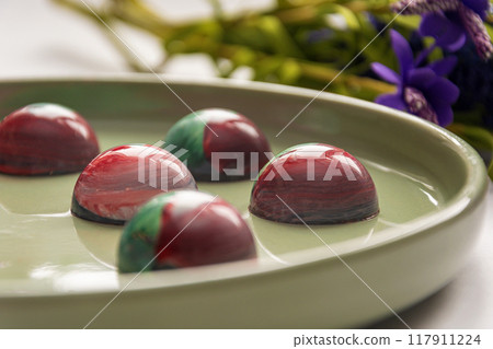 Collectible handmade tempered chocolate candies with a glossy painted body on a round plate with a blurred background and bokeh elements 117911224