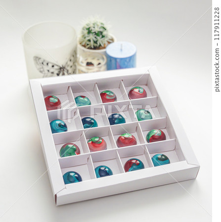 Tempered chocolate candies with glossy painted body in a box with blurred background and bokeh elements 117911228