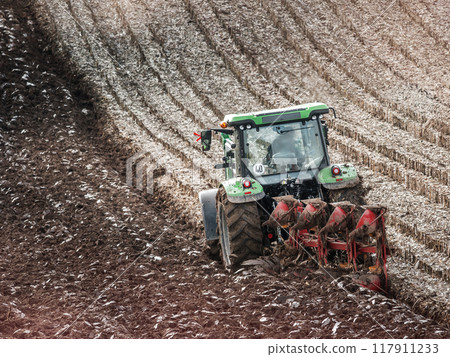 Farm tractor furrowing arable field 117911233