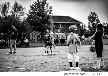 Two youth softball girls at first base with defocused coach and team in background. 117914115