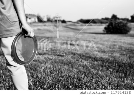 Selective focus fairway grass with a defocused young child holding a putter disc and golf goal in the distance. Selective focus fairway grass with a defocused young child holding a putter disc and golf goal in the distance. 117914128