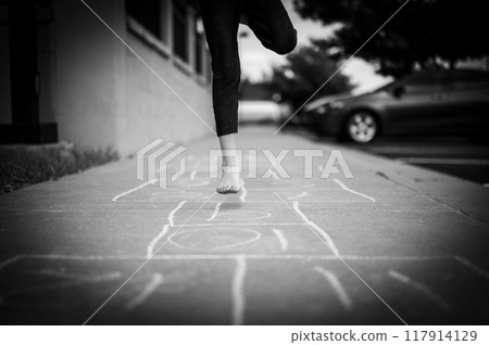 Selective focus on chalk numbers with a girl playing hop-scotch barefoot 117914129