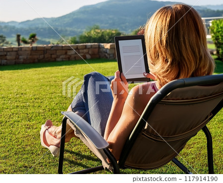 A woman relaxing outdoors with an e-reader in the afternoon sun surrounded by mountains. Generative AI A woman relaxing outdoors with an e-reader in the afternoon sun surrounded by mountains. Generative AI 117914190