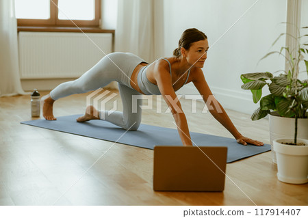 Dedicated Fitness Enthusiast Actively Practicing Yoga at Home Using Laptop for Guidance Dedicated Fitness Enthusiast Actively Practicing Yoga at Home Using Laptop for Guidance 117914407