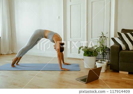 A woman practices yoga at home in her modern living room, creating a serene environment A woman practices yoga at home in her modern living room, creating a serene environment 117914409