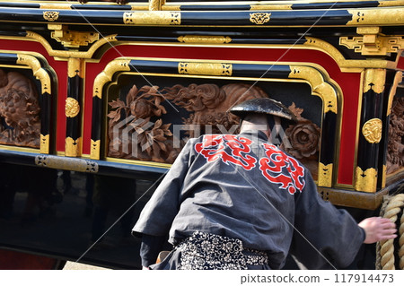 Takayama City, Gifu Prefecture, Japan: Spring Takayama Festival: Men carrying gorgeous floats called yatai, wearing happi coats and jinbaori hats, seen from behind Takayama City, Gifu Prefecture, Japan: Spring Takayama Festival: Men carrying gorgeous floats called yatai, wearing happi coats and jinbaori hats, seen from behind 117914473