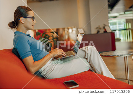 A professional woman is diligently working on her laptop in a modern workspace environment A professional woman is diligently working on her laptop in a modern workspace environment 117915206