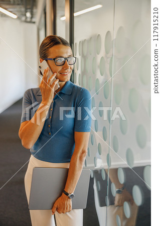 A professional woman is conversing on her phone in a sleek, modern office environment 117915210
