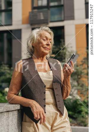 An Elegant Senior Woman Joyfully Using Her Smartphone in a Bustling Urban Setting An Elegant Senior Woman Joyfully Using Her Smartphone in a Bustling Urban Setting 117915247