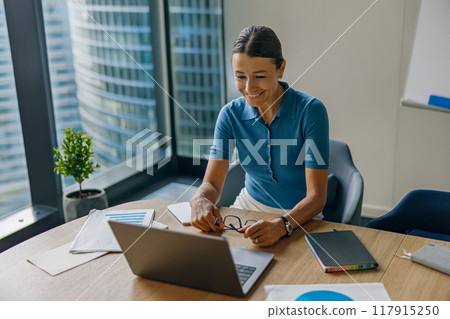 A professional woman is working intently on her laptop in a modern office environment 117915250