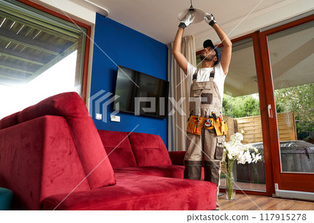 Male electrician finished mounting ceiling lamp - installing a fluorescent light bulb 117915278