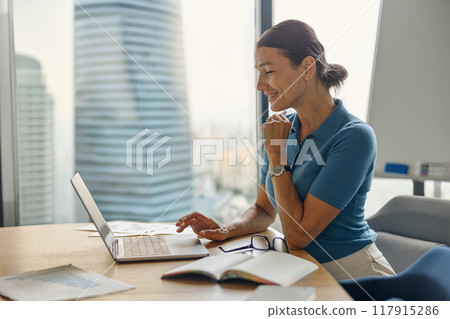 A Professional Woman is Focusing on Her Work While Using a Laptop in a Modern Office Setting 117915286