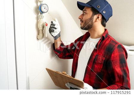 Male plumber is checking water meter and making notes in tablet at home. High quality photo 117915291