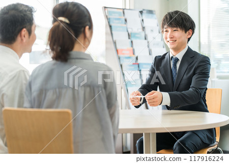 一位年輕的亞洲商人和一對客戶夫婦在陳列室/商務談判空間遞出名片 117916224