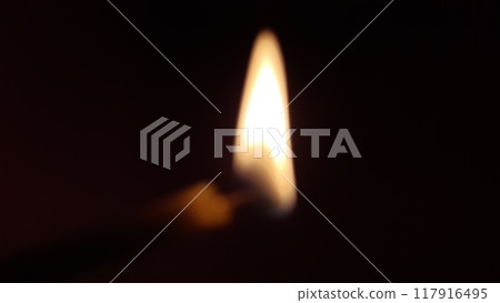 Burning candle in the dark, out of focus. The edge of the candle is slightly visible near the flame, and the flickering of the fire appears to me as a slight blur. 117916495