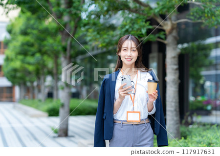 A businesswoman walking through a business district with a smartphone 117917631