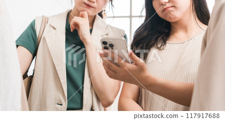A female customer looking at her smartphone while shopping at an apparel store 117917688