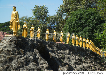 Beautiful statues of Buddha and monks holding alms bowls line up at Mahamuni Phya temple. It is located on the Rakhine State, Myanmar. 117921527