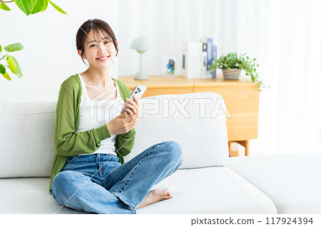 A young woman operating a smartphone in a room 117924394