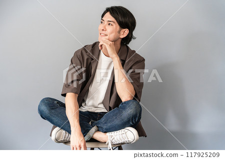 一個穿著運動鞋和牛仔褲的清爽男人坐在椅子上 117925209