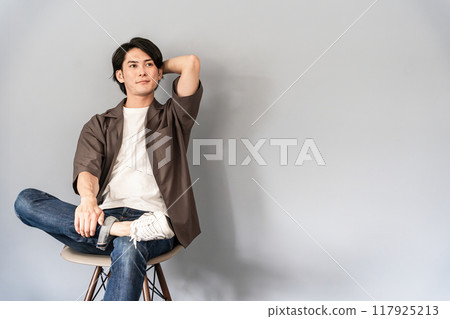 A refreshing man wearing sneakers and jeans sitting on a chair 117925213
