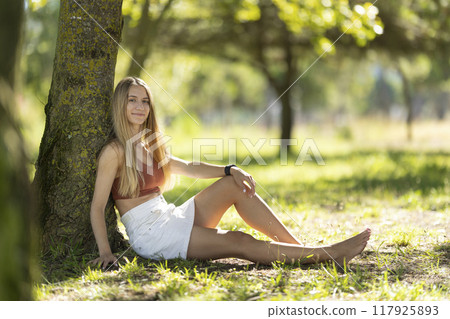 Young woman relaxing under tree in a park Young woman relaxing under tree in a park 117925893