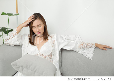 A woman in a white nightgown appears distressed by a headache during the night. 117927235