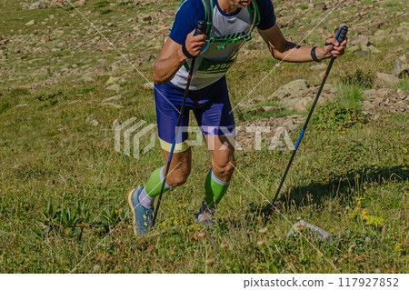athlete with trekking poles climbing significant ascent during mountain marathon 117927852