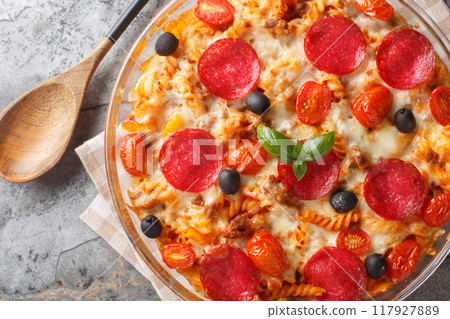 Pizza Casserole of tender pasta, browned beef meat, salami, olives, bell peppers and cheese smothered in marinara sauce closeup on the in a glass bowl. Horizontal top view Pizza Casserole of tender pasta, browned beef meat, salami, olives, bell peppers and cheese smothered in marinara sauce closeup on the in a glass bowl. Horizontal top view 117927889