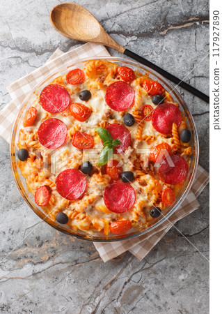 Pizza casserole Pasta baked in a tomato sauce with cheese, sausages, peppers and olives closeup on the in a glass bowl. Vertical top view Pizza casserole Pasta baked in a tomato sauce with cheese, sausages, peppers and olives closeup on the in a glass bowl. Vertical top view 117927890