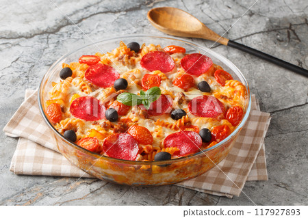 Pasta pizza casserole with cheese, fried ground beef, salami sausage, peppers and olives with marinara sauce close-up in glass baking dish. Horizontal Pasta pizza casserole with cheese, fried ground beef, salami sausage, peppers and olives with marinara sauce close-up in glass baking dish. Horizontal 117927893