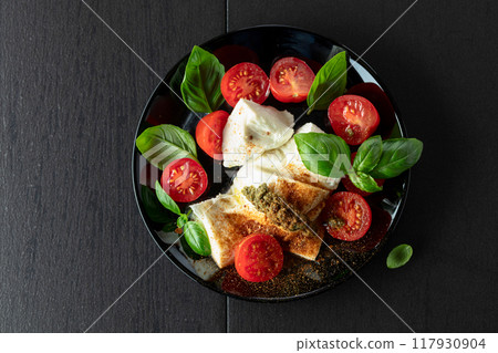 Mozzarella with basil, cherry tomatoes and pesto sauce sprinkled with spices. 117930904